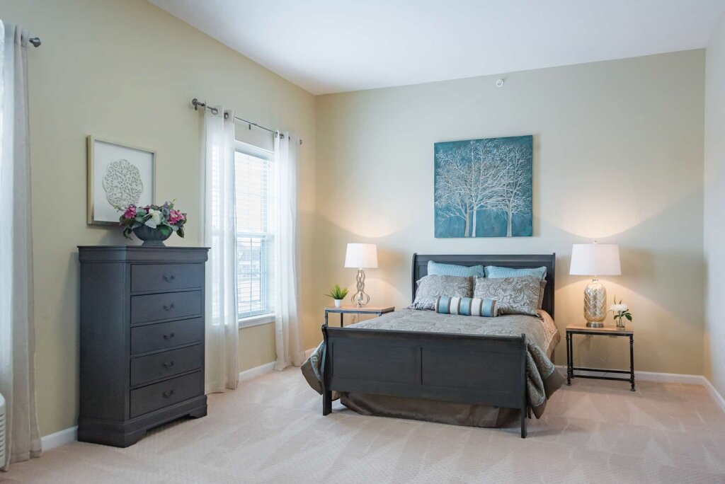 Furnished senior apartment bedroom at Traditions at Brookside features a dark wood bed frame and a matching tall dresser.