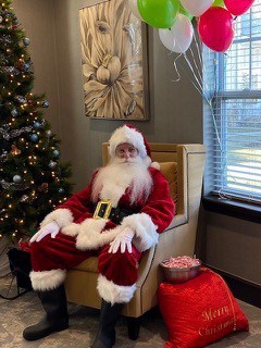 Santa is seated next to the tree and his bag of goodies