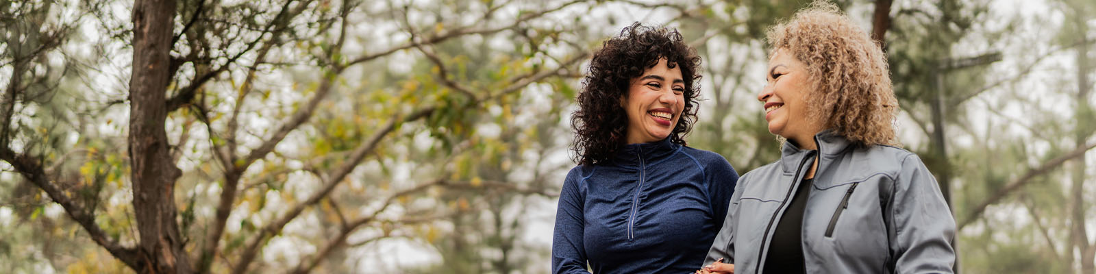 A mature woman and her daughter walking outdoors in a park while smiling at each other