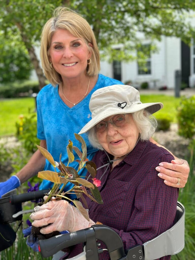 Resident and team member smile together after planting flowers in the community garden at Traditions at Brookside.