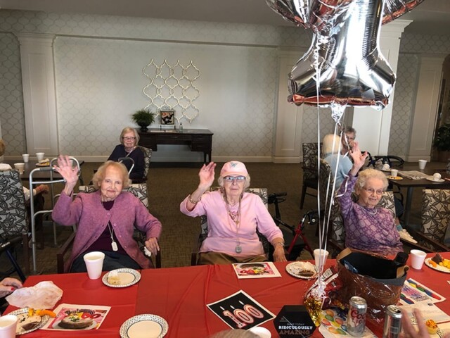 Three elderly women raise their hands while taking a photo